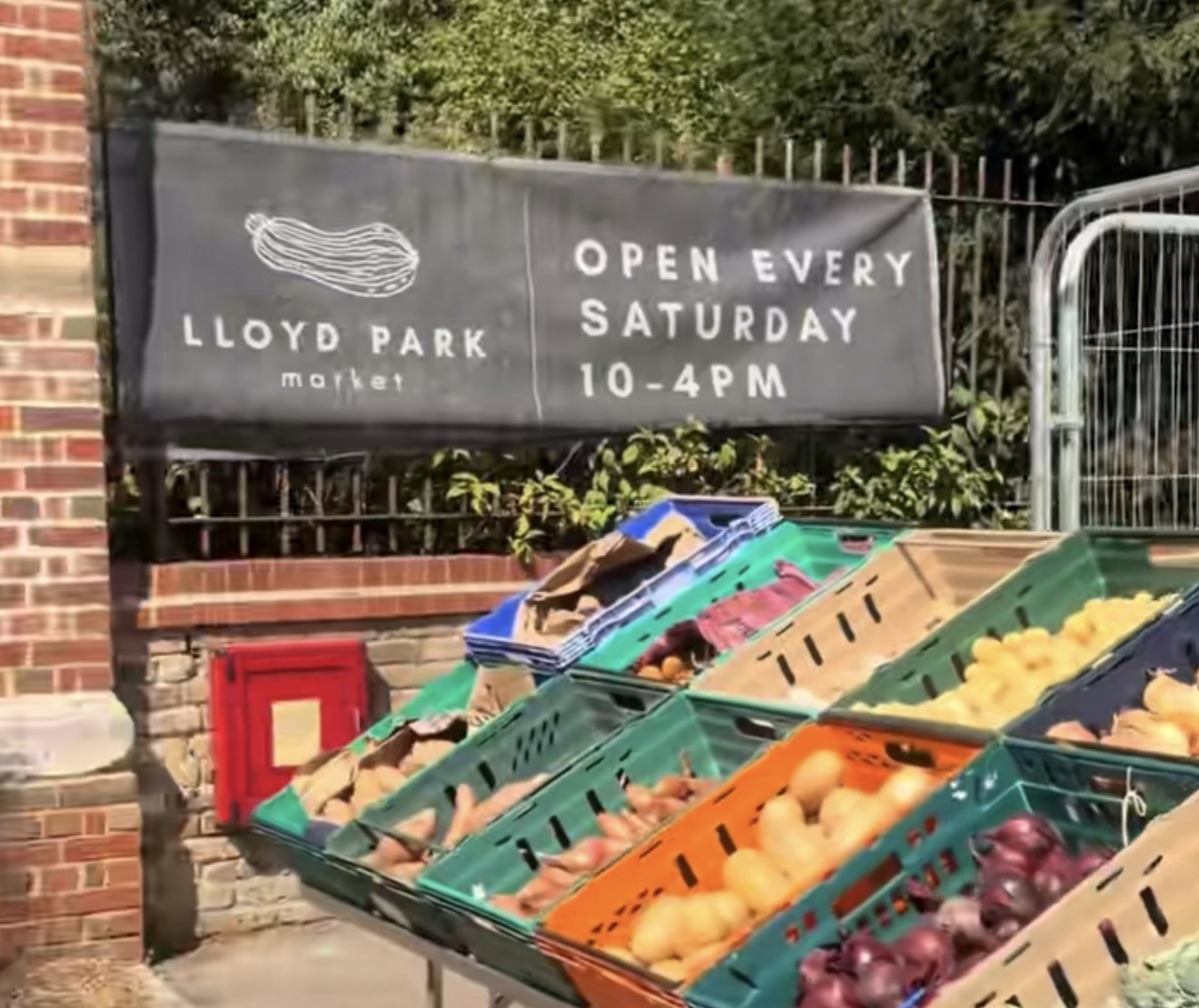 Lloyd Park Market banner reading open every Saturday 10 to 4pm above fruit and vegetable crates