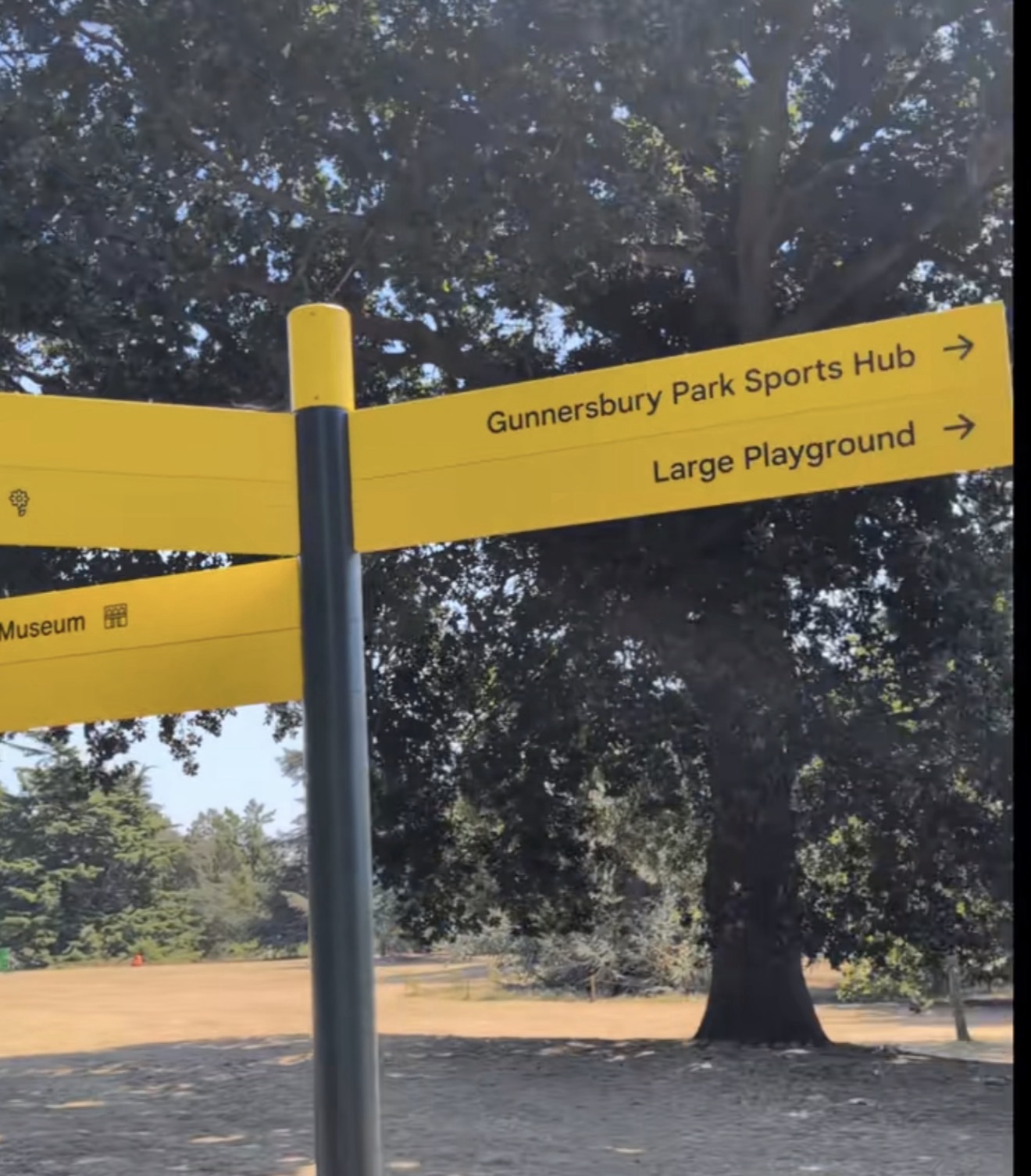 Yellow signpost pointing to Gunnersbury Park Sports Hub, the Large Playground and the Museum