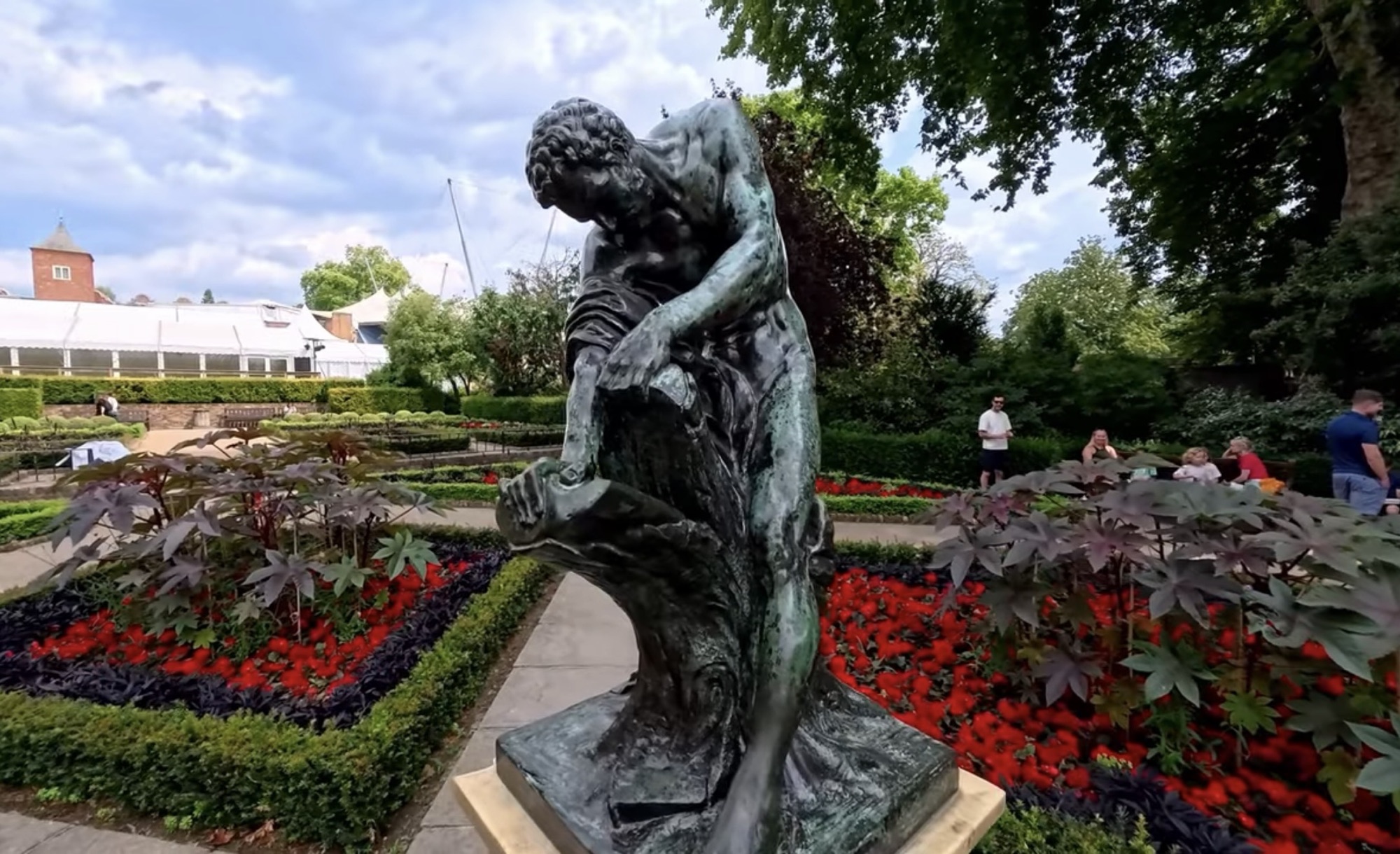 Close view of the Milo of Croton statue with red flower beds in the Dutch Garden
