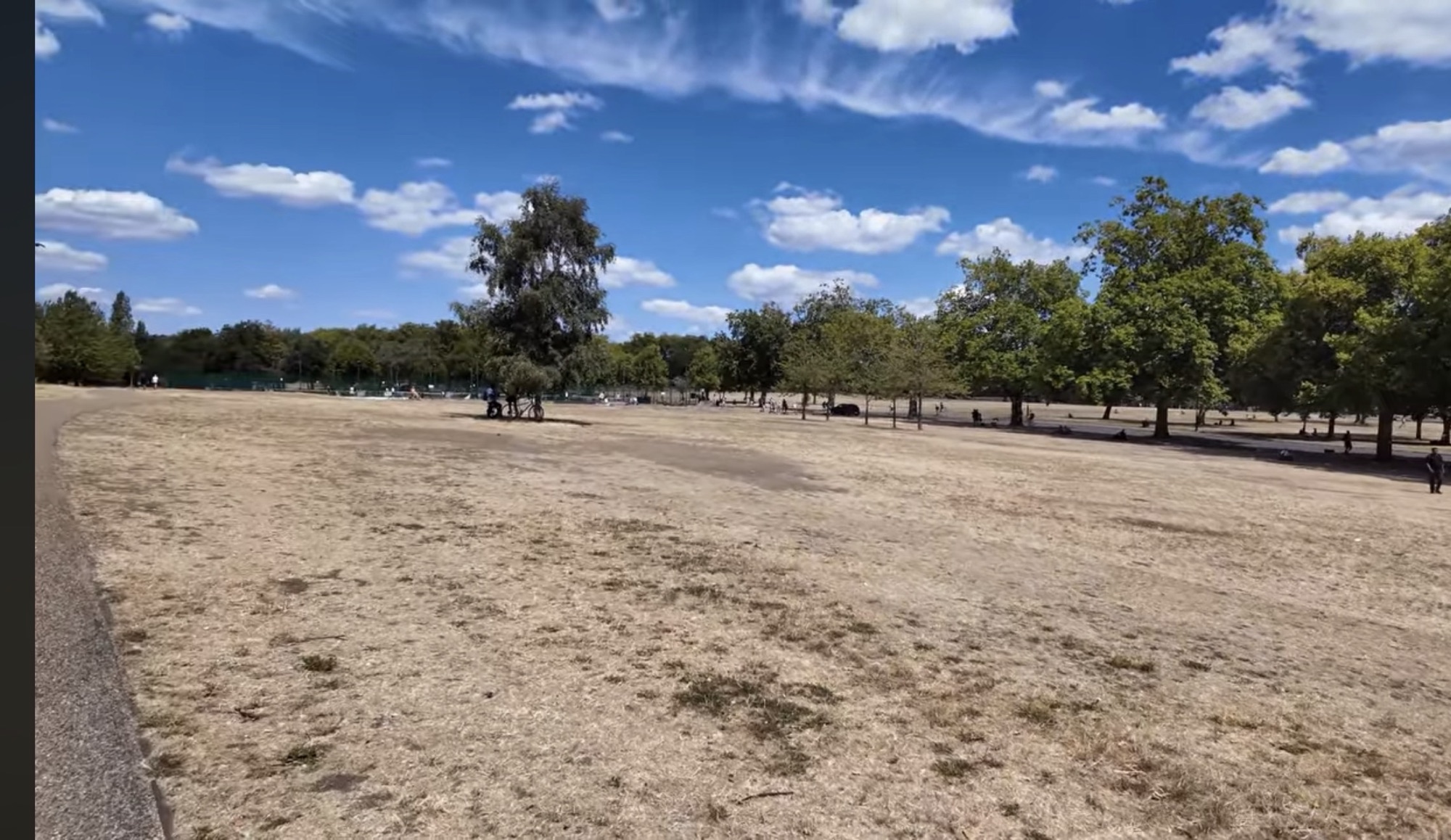 Open parkland in Finsbury Park with a cyclist resting beneath a tree