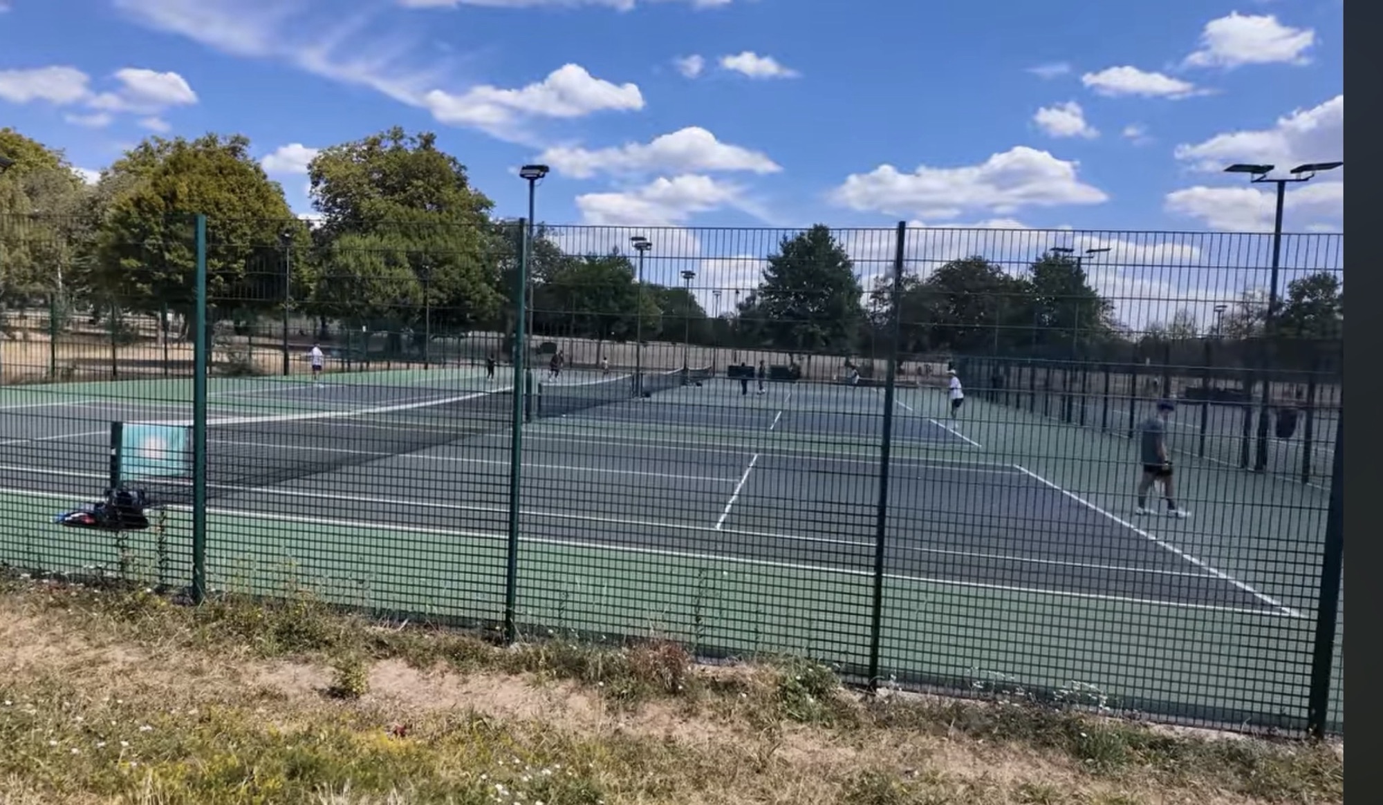 Players on the floodlit tennis courts in Finsbury Park on a sunny day
