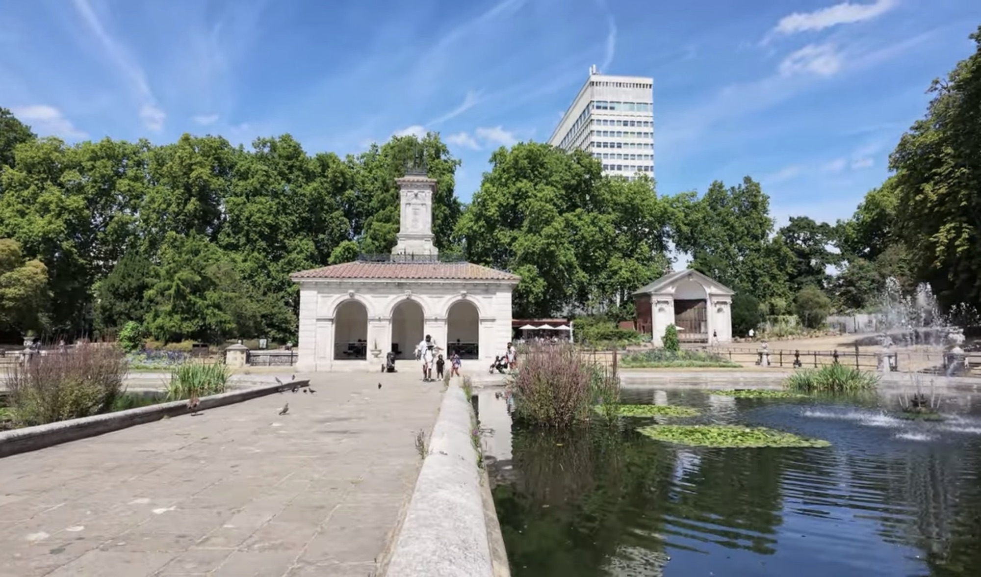 The Italian Gardens pump house and clock tower seen across the lily pond, with a tower block behind the trees
