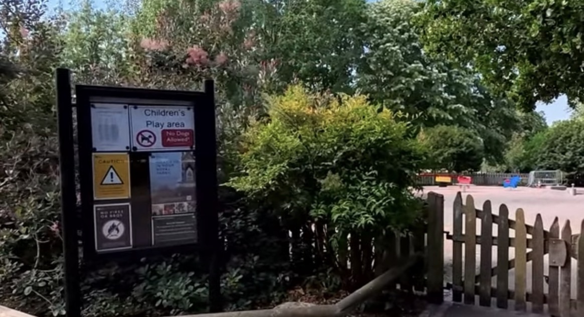 Children's Play Area sign with no-dogs and caution notices fixed beside a wooden playground gate