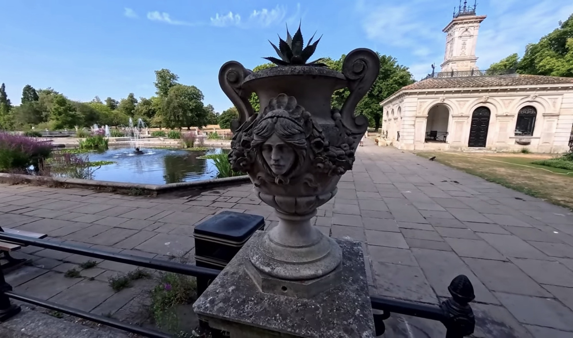 Carved stone urn with a mascaron face on the Italian Gardens balustrade, with the pump house building behind