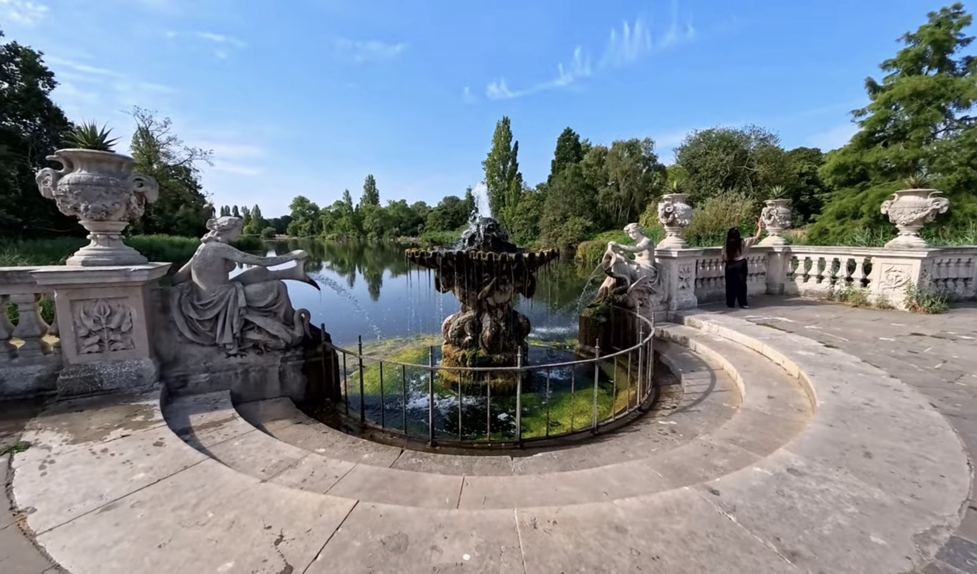 Wide view of the Italian Gardens fountain, stone balustrade and reclining figures overlooking the Long Water