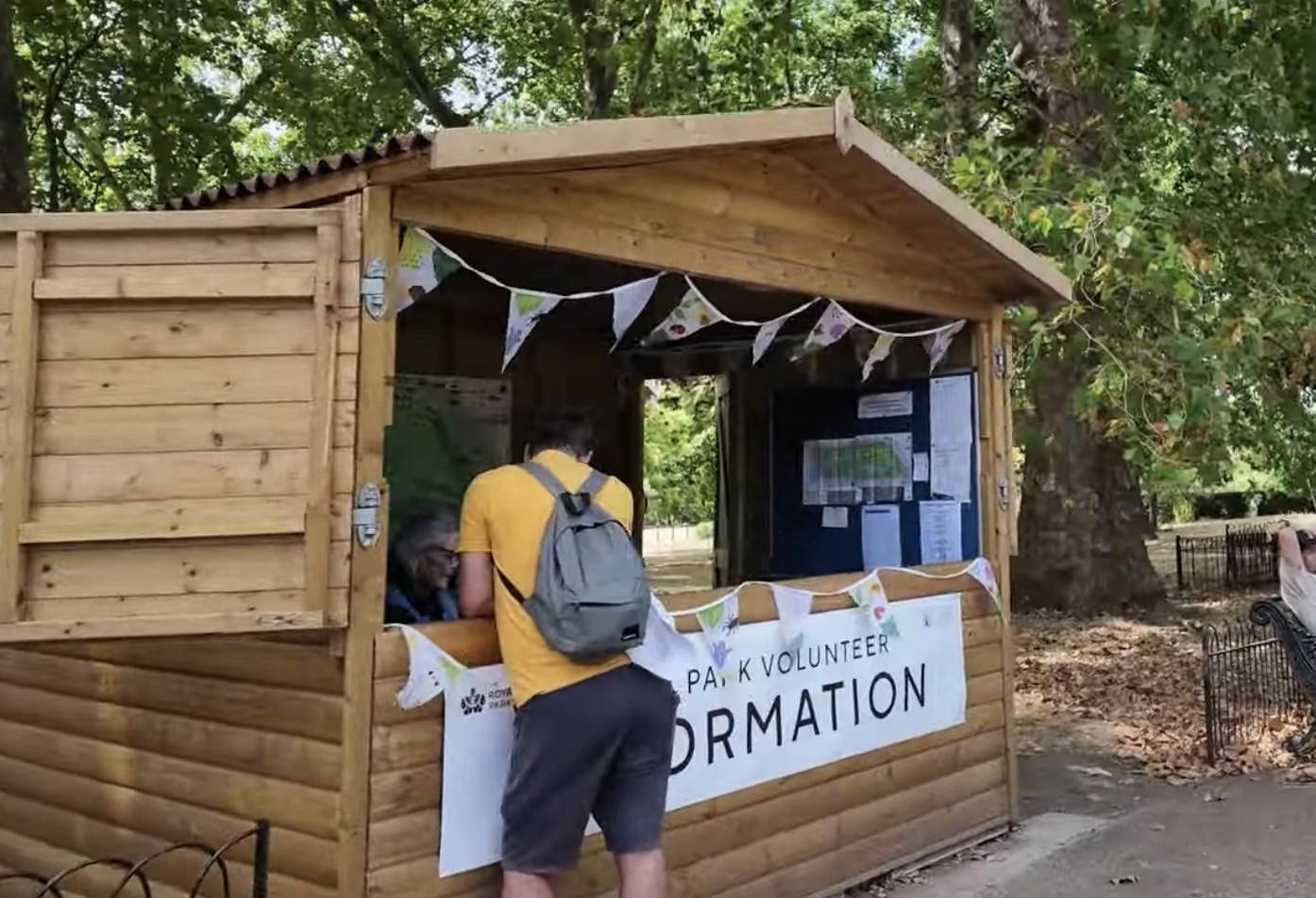 Wooden Park Volunteer Information hut in Hyde Park with bunting and a visitor asking for directions