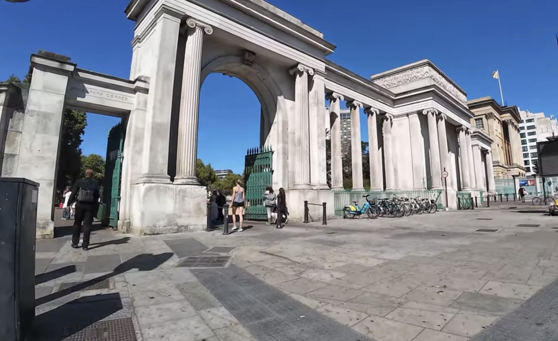 Wide view of the colonnaded stone screen and archway at Hyde Park Corner with cyclists and pedestrians passing through