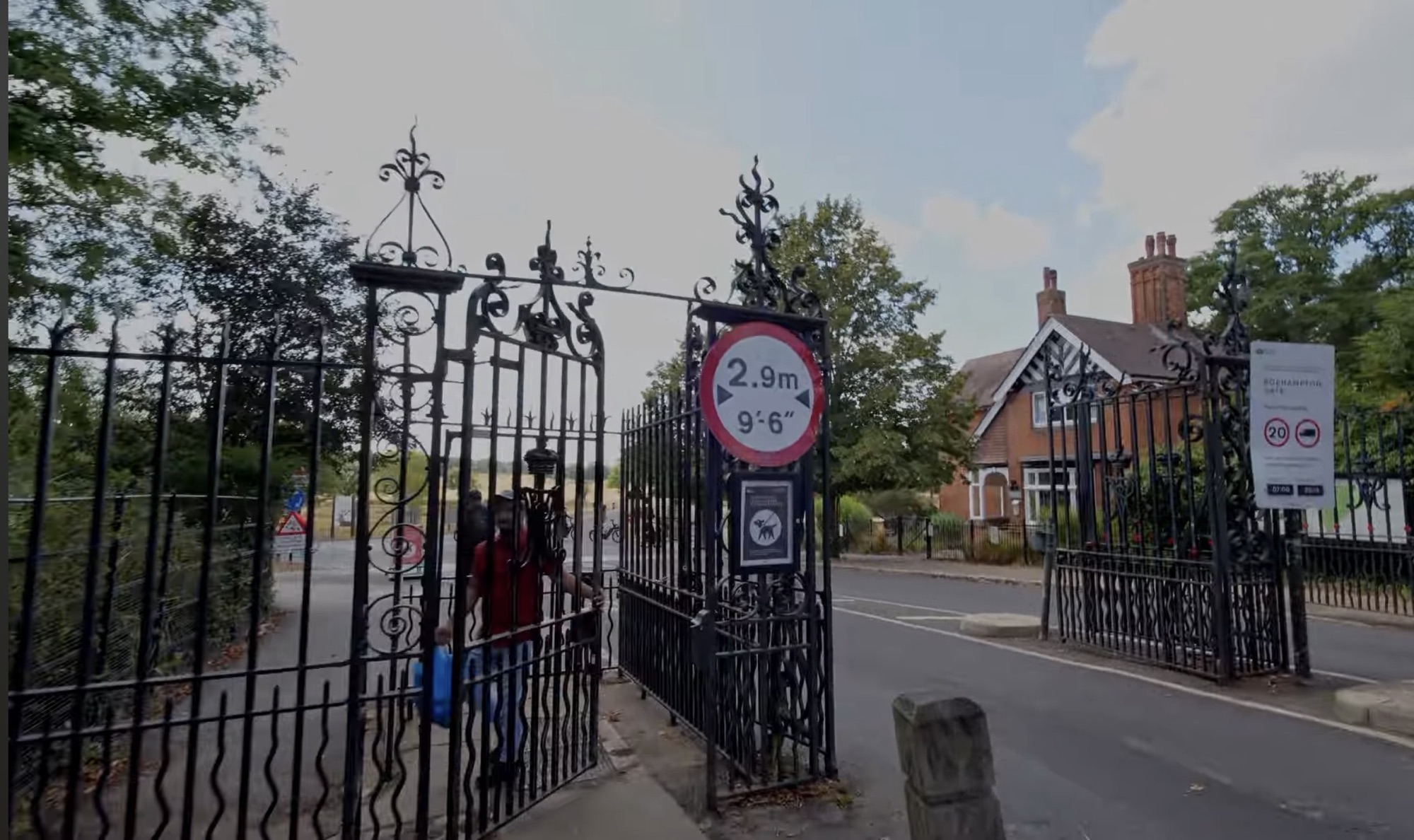 Ornate wrought iron gates at Roehampton Gate in Richmond Park with a vehicle width restriction sign
