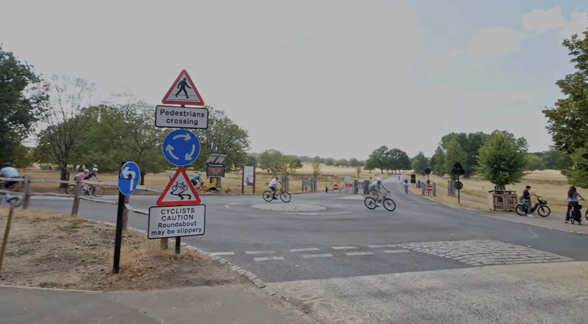 Cyclists crossing a roundabout in Richmond Park with pedestrian crossing and cyclist caution signs in the foreground