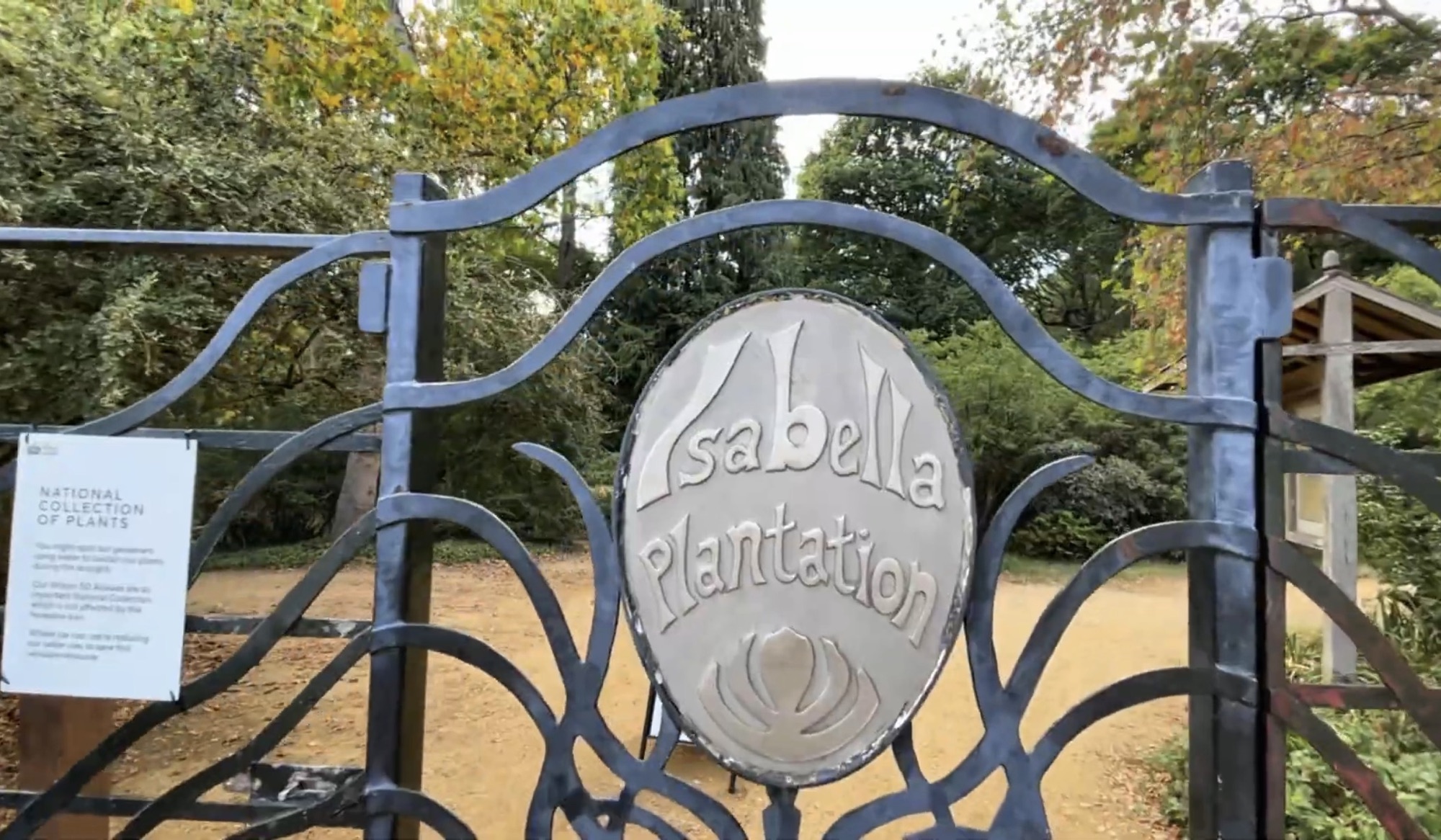 Ornate metal gate reading Isabella Plantation with a National Collection of Plants sign beside it