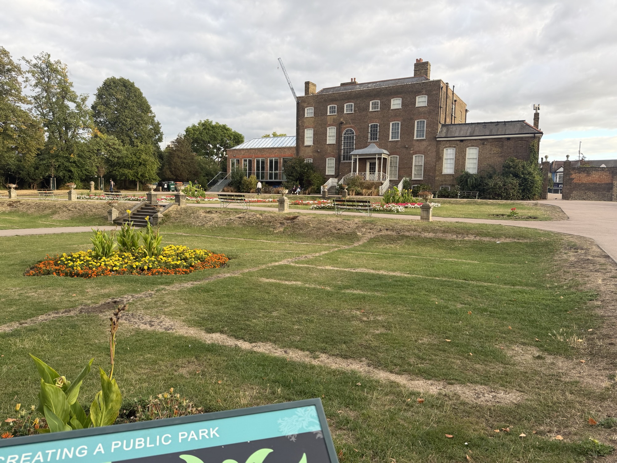 Open lawn and flowerbeds in front of the William Morris Gallery at Lloyd Park, with benches along the paths