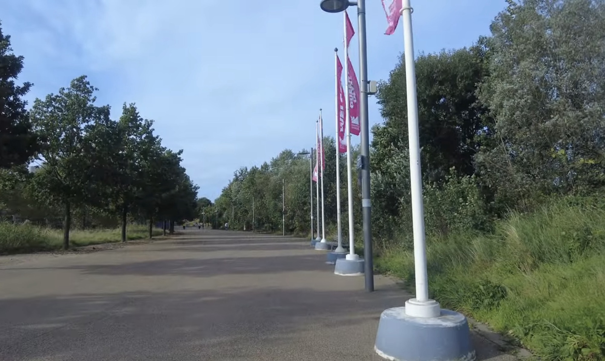 Tree-lined path with pink flags along a wide walkway in Queen Elizabeth Olympic Park