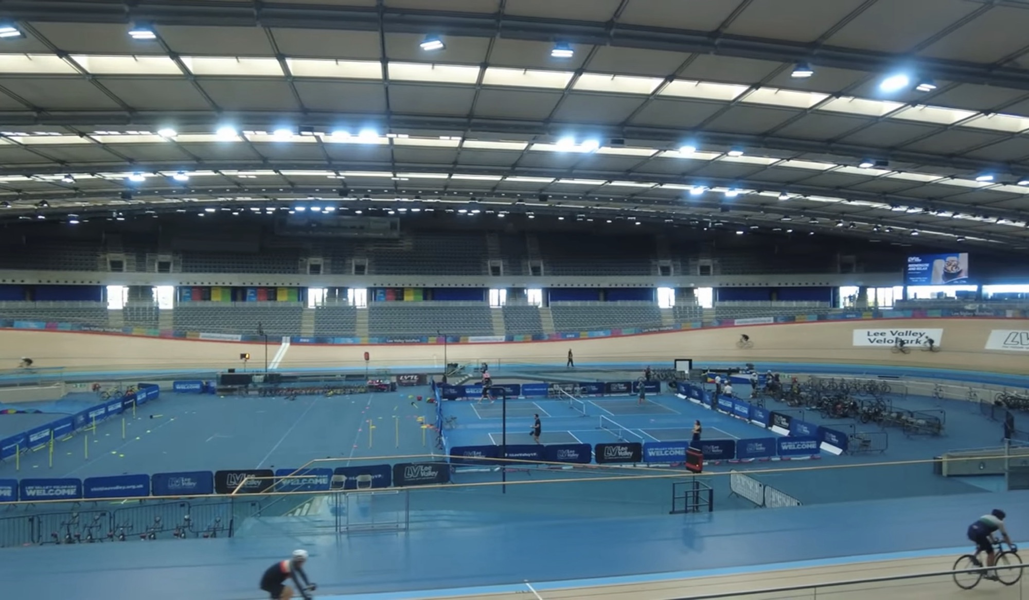 Cyclists on the track and tennis courts inside the Lee Valley VeloPark velodrome at Queen Elizabeth Olympic Park