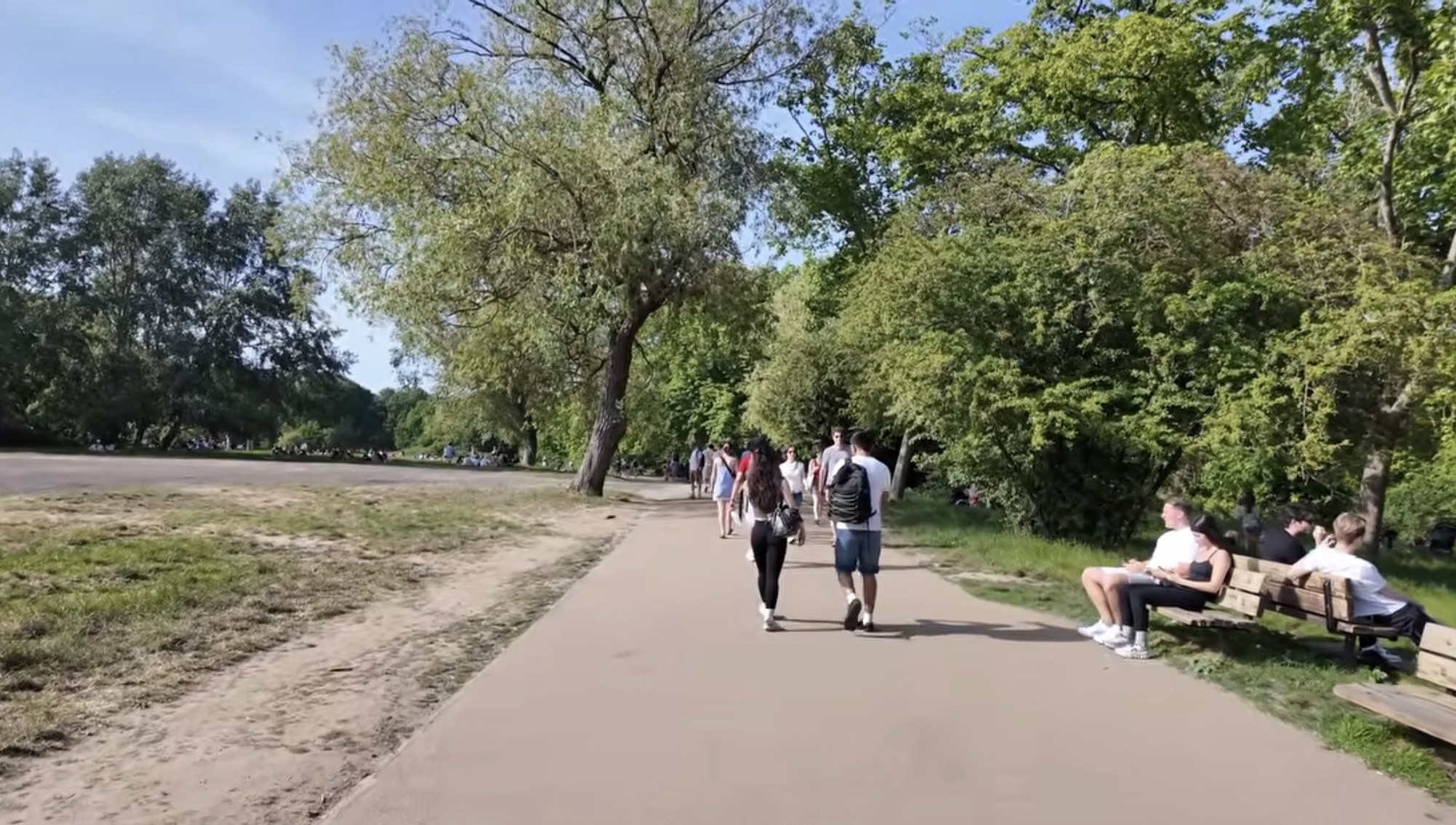 Wide sandy path with people walking and sitting on benches at Hampstead Heath