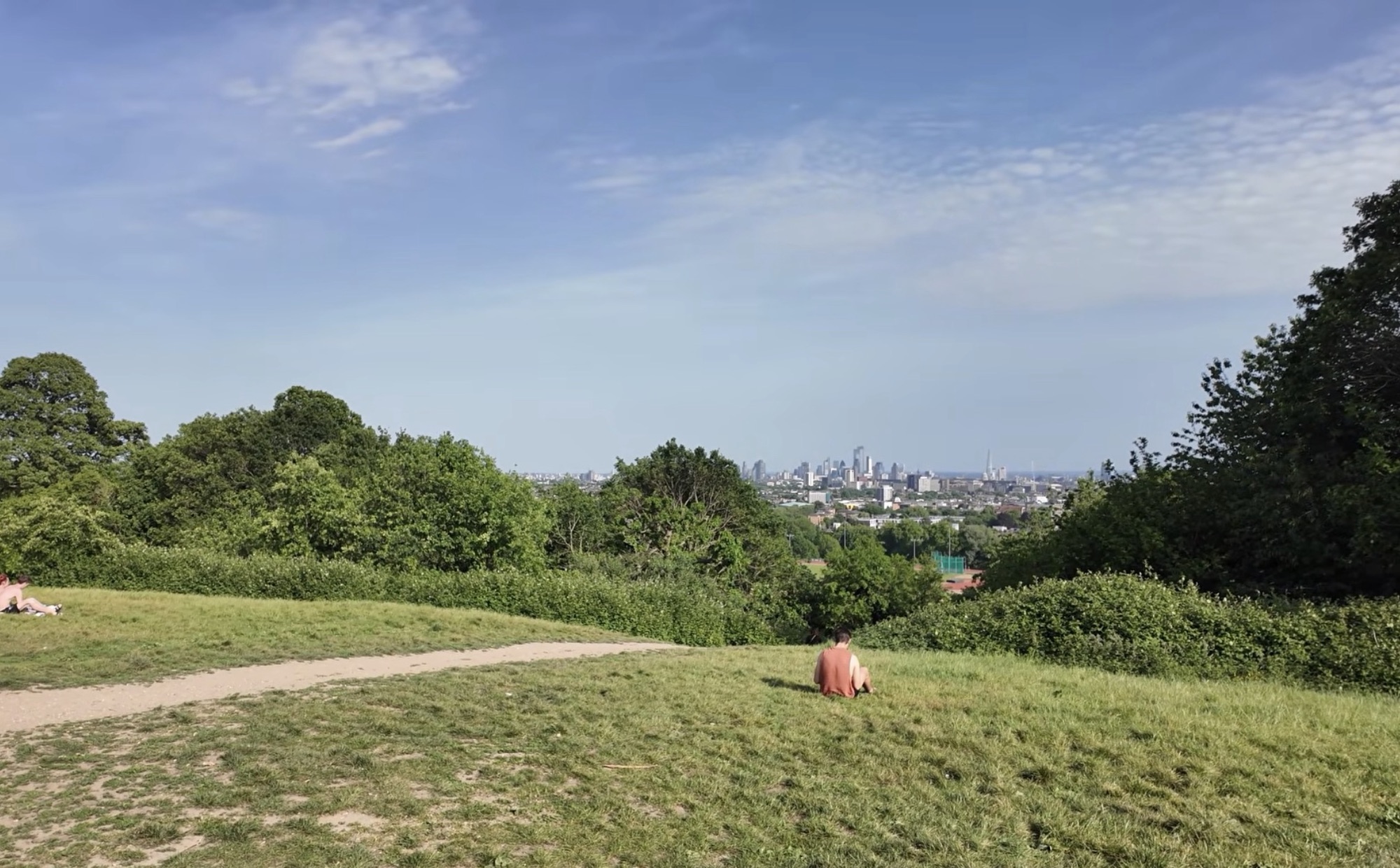 Person sitting on the grass on a hilltop at Hampstead Heath with the City of London skyline visible in the distance
