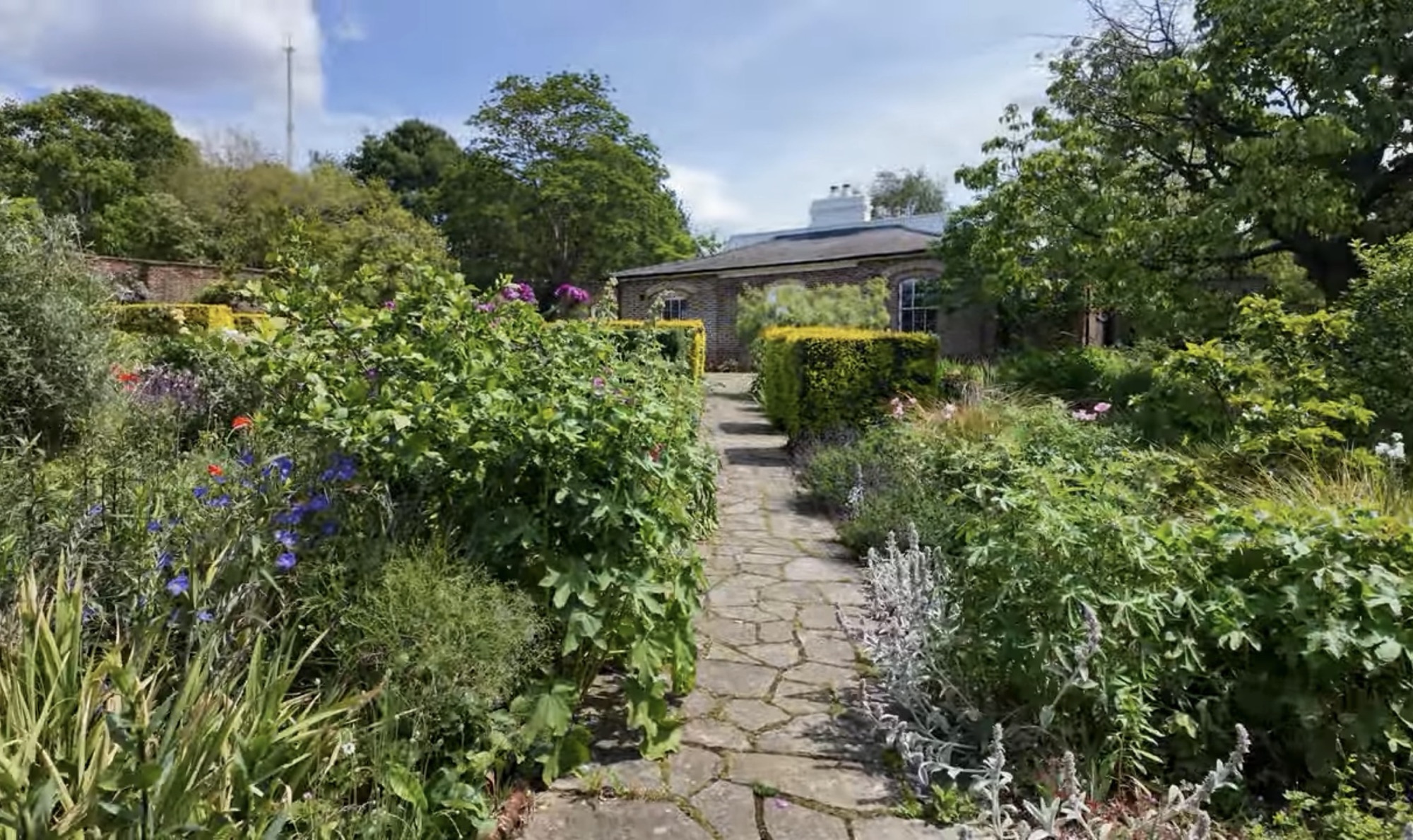 Stone path through flower beds and hedges leading towards a brick building inside the Walled Garden at Brockwell Park