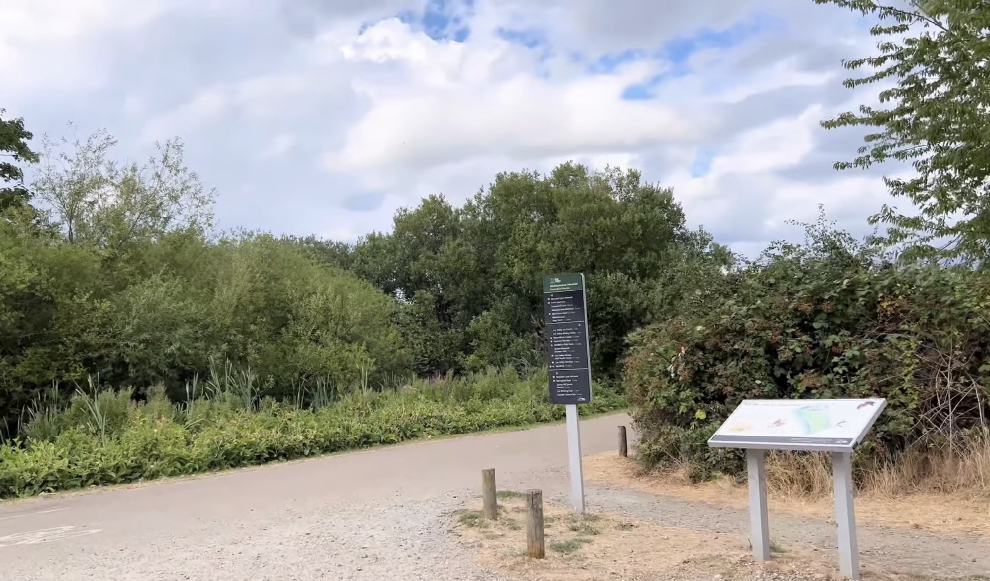 Path junction with a waymarker sign and information board surrounded by greenery