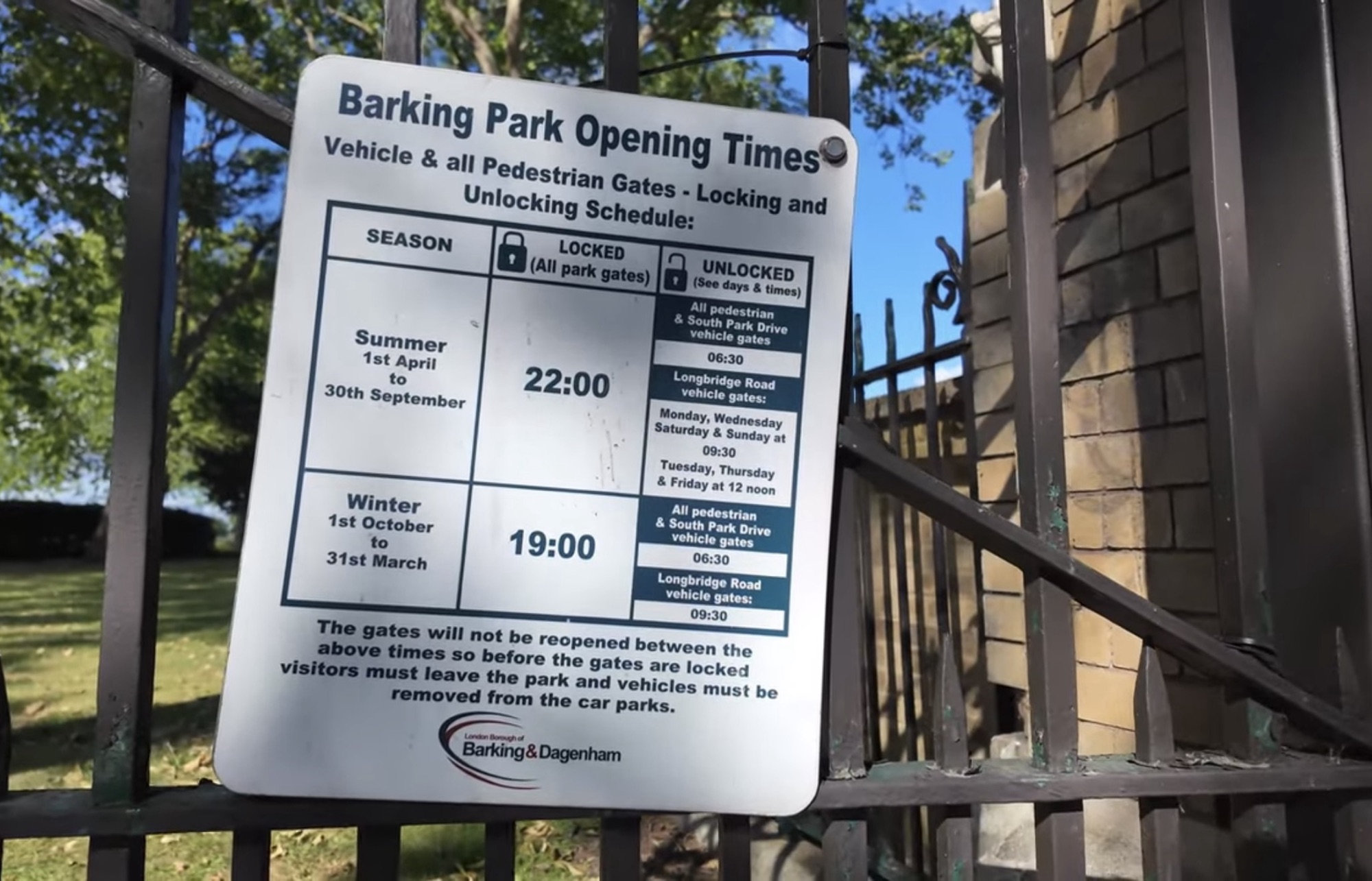 Barking Park opening times sign on the entrance gate showing summer and winter locking times