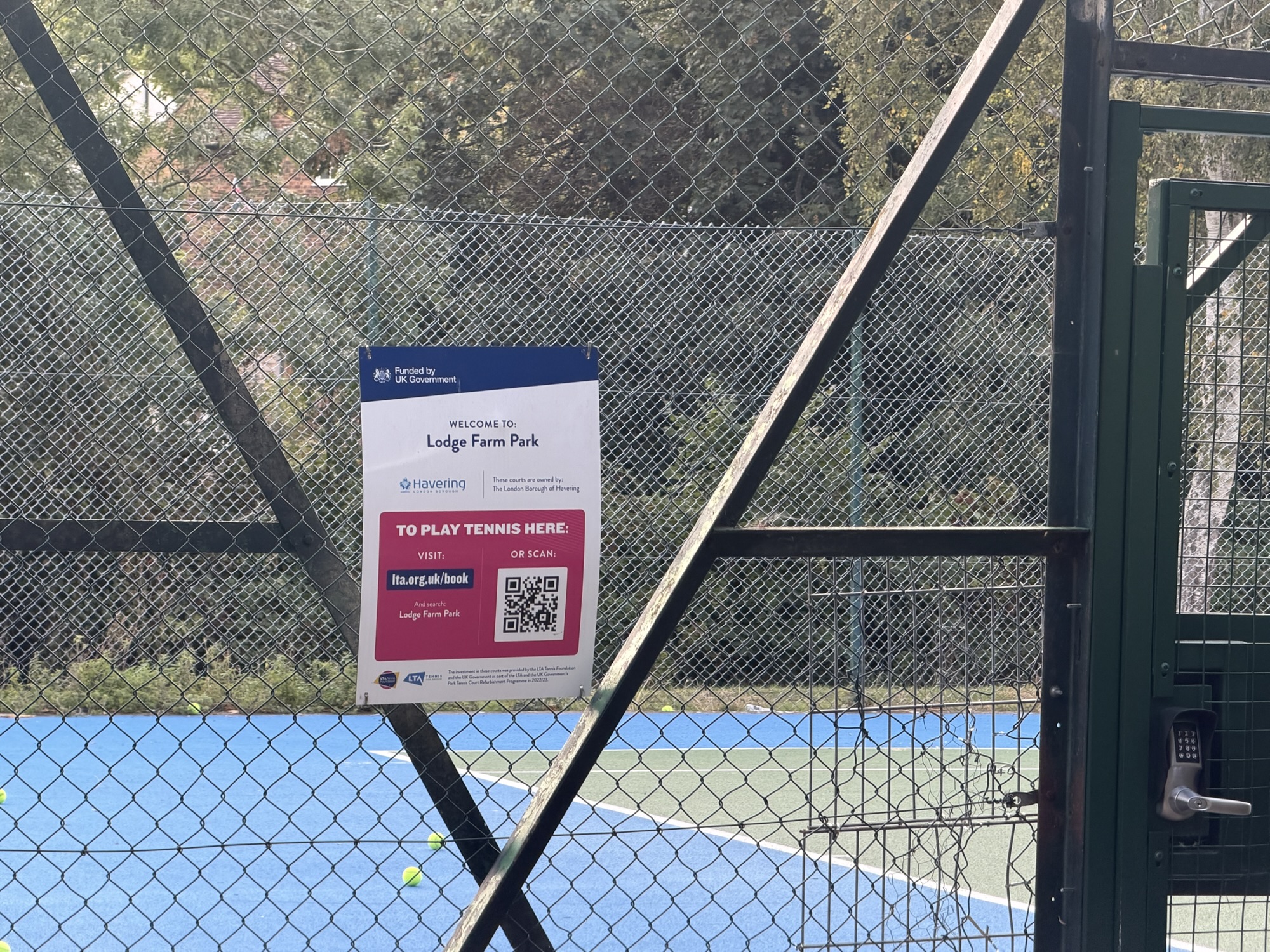 Sign on the tennis court fence welcoming visitors to Lodge Farm Park with booking details