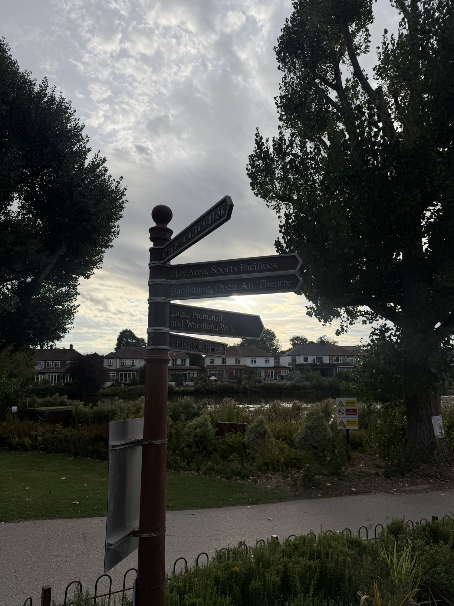 Wooden fingerpost signage pointing to the cafe, play area, bandstand, lake and car park in Raphael Park
