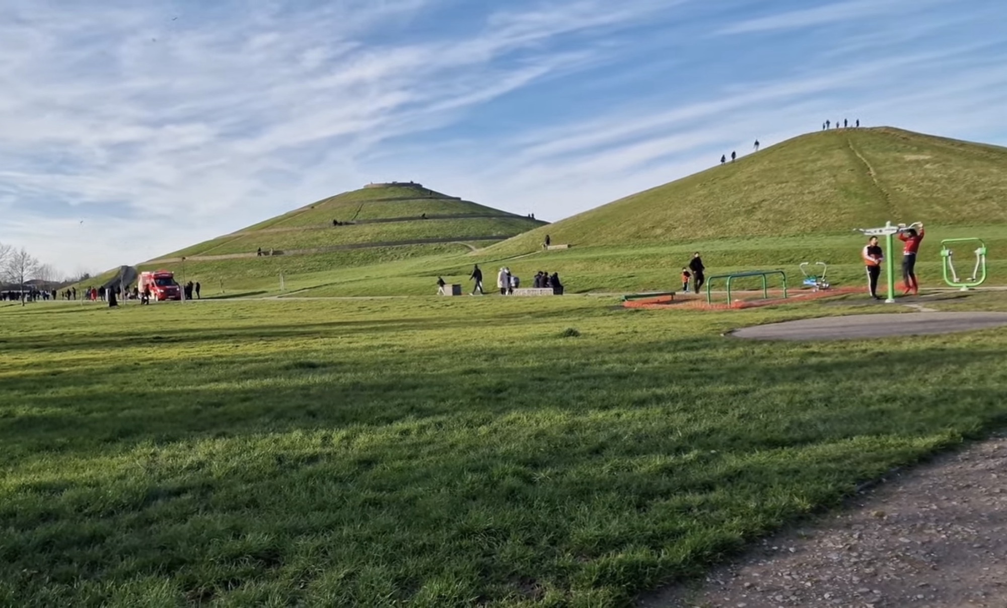 Outdoor gym equipment and open grass with two man-made hills behind at Northala Fields