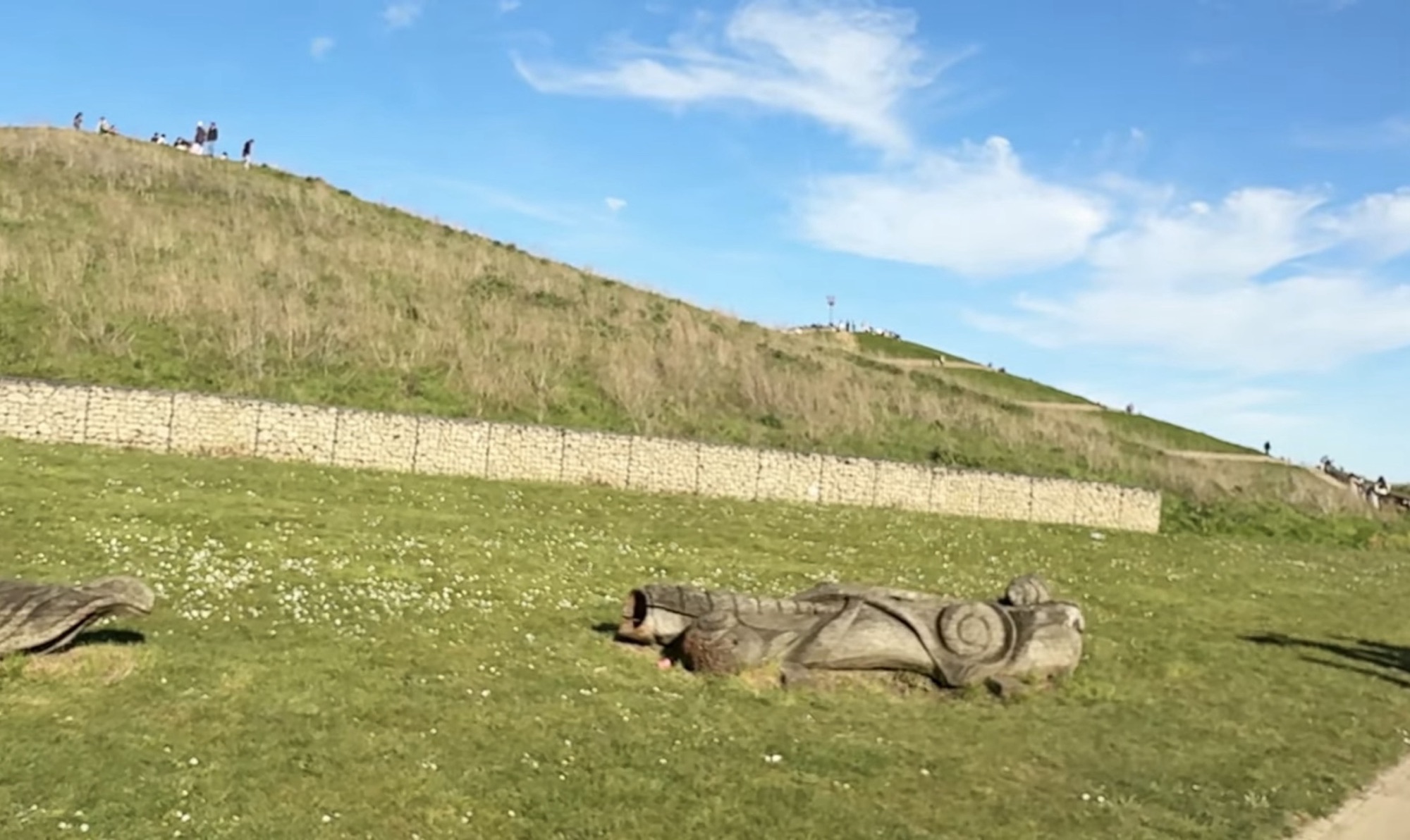 Wooden carved log sculptures on grass below a grassy man-made hill at Northala Fields