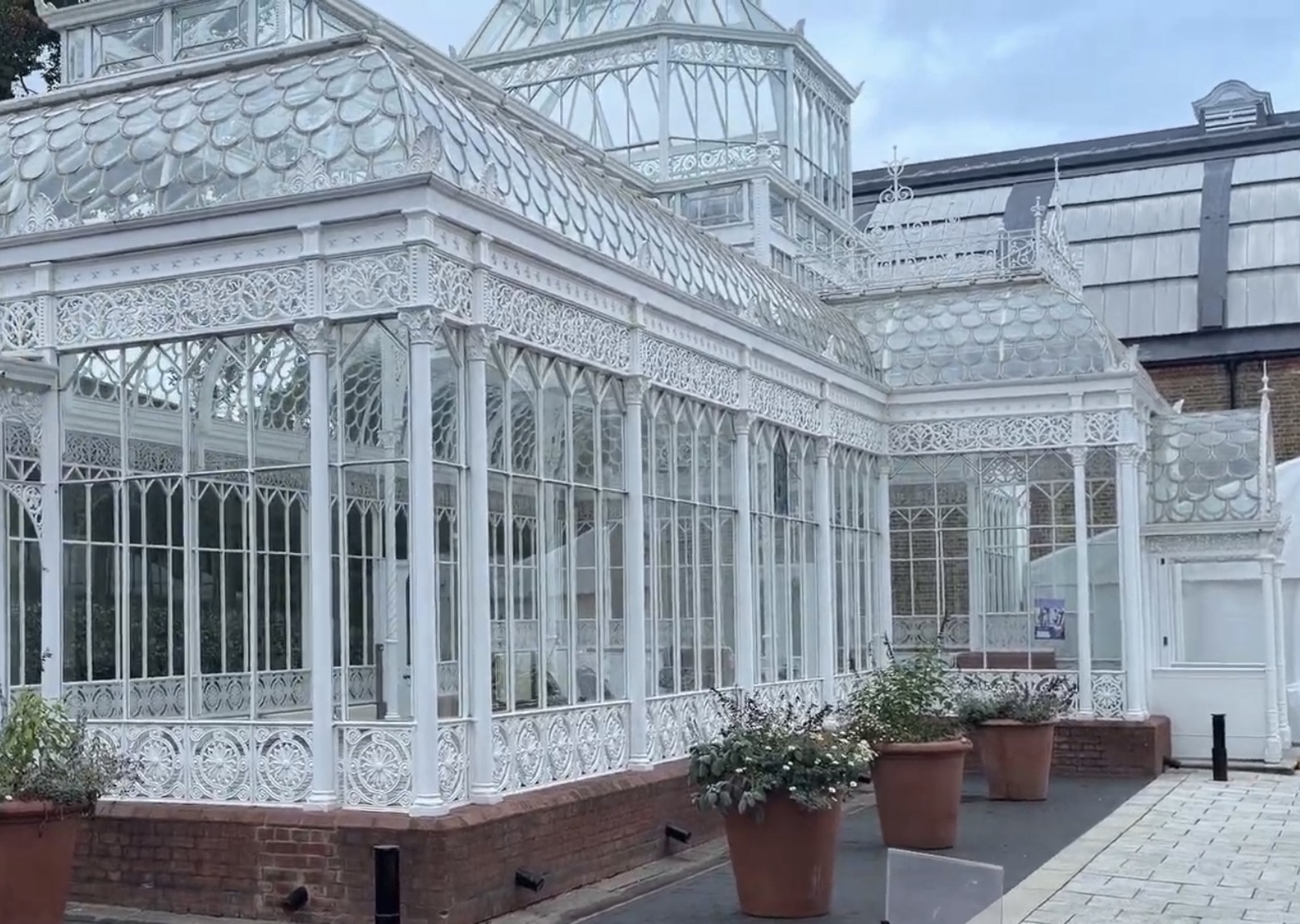 White ornate Victorian glass conservatory in the Horniman Gardens with potted plants outside
