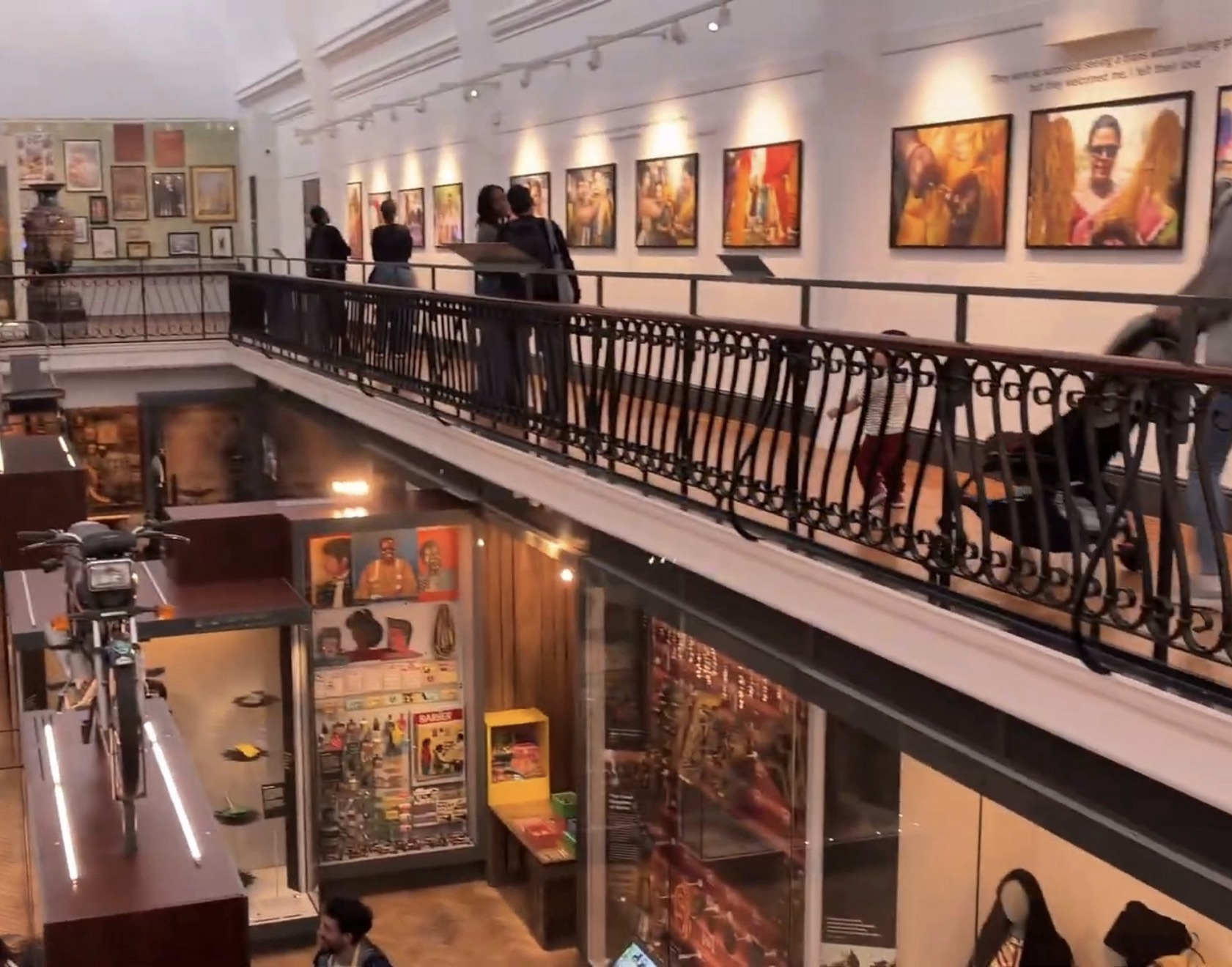Interior of the World Gallery at the Horniman Museum with a balcony, framed portraits and display cases below
