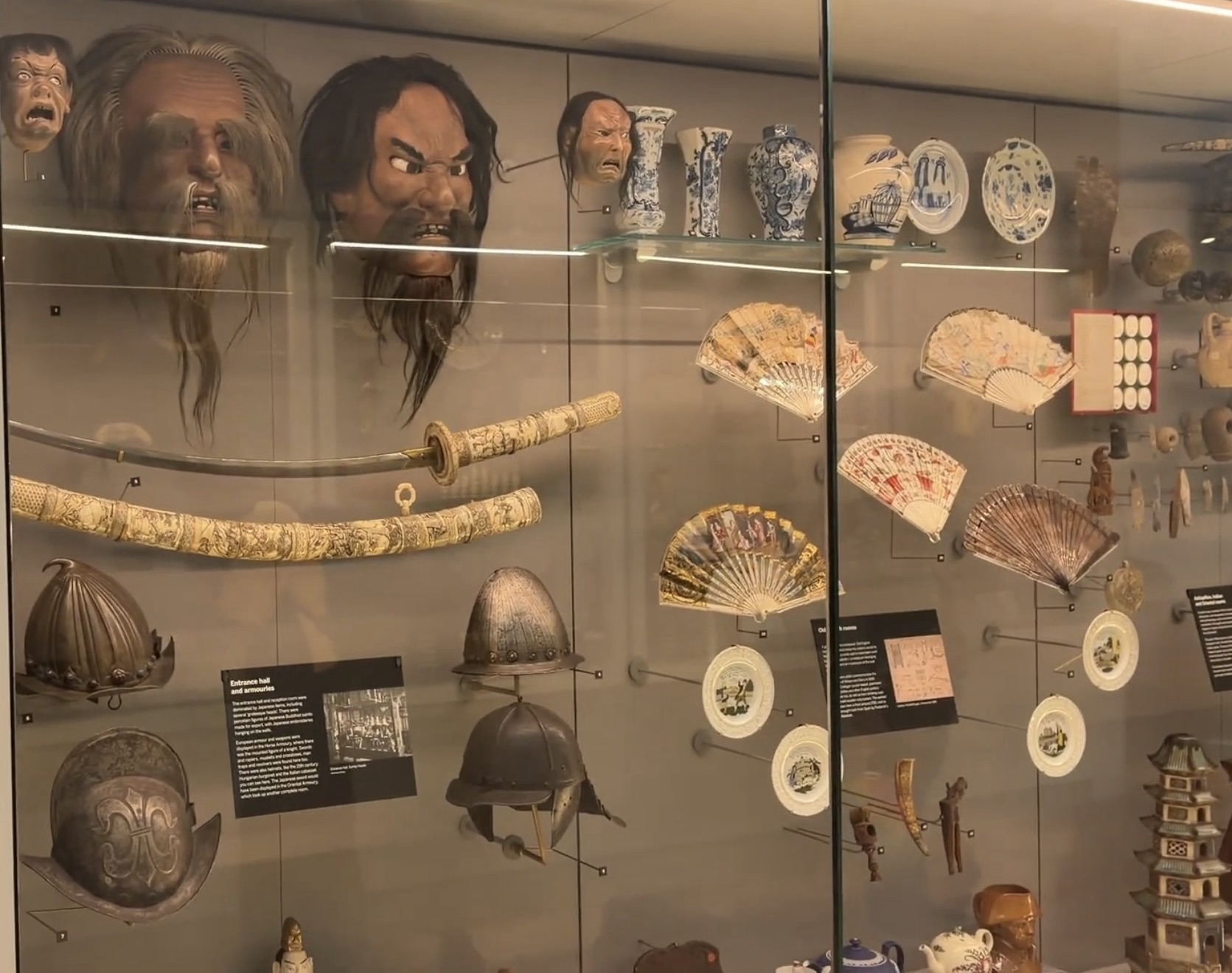 Display case at the Horniman Museum with Japanese masks, a carved sword, fans, helmets and ceramics