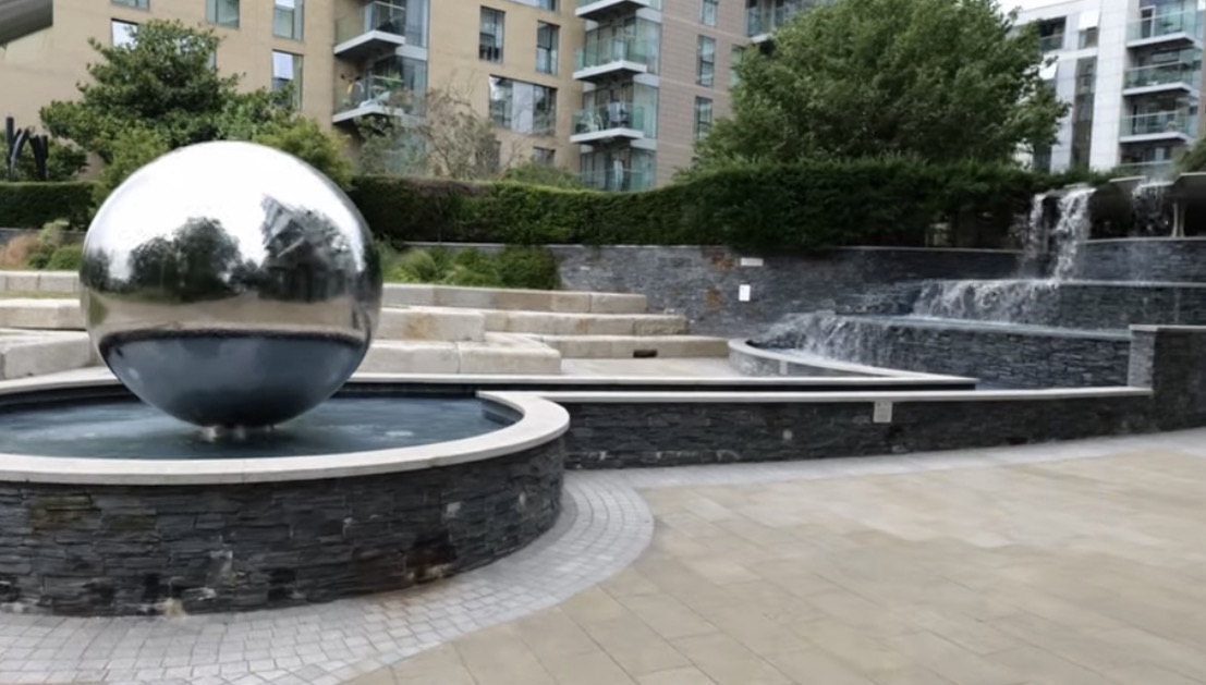 Polished steel sphere in a round fountain beside a stepped slate waterfall and apartment blocks in Woodberry Down