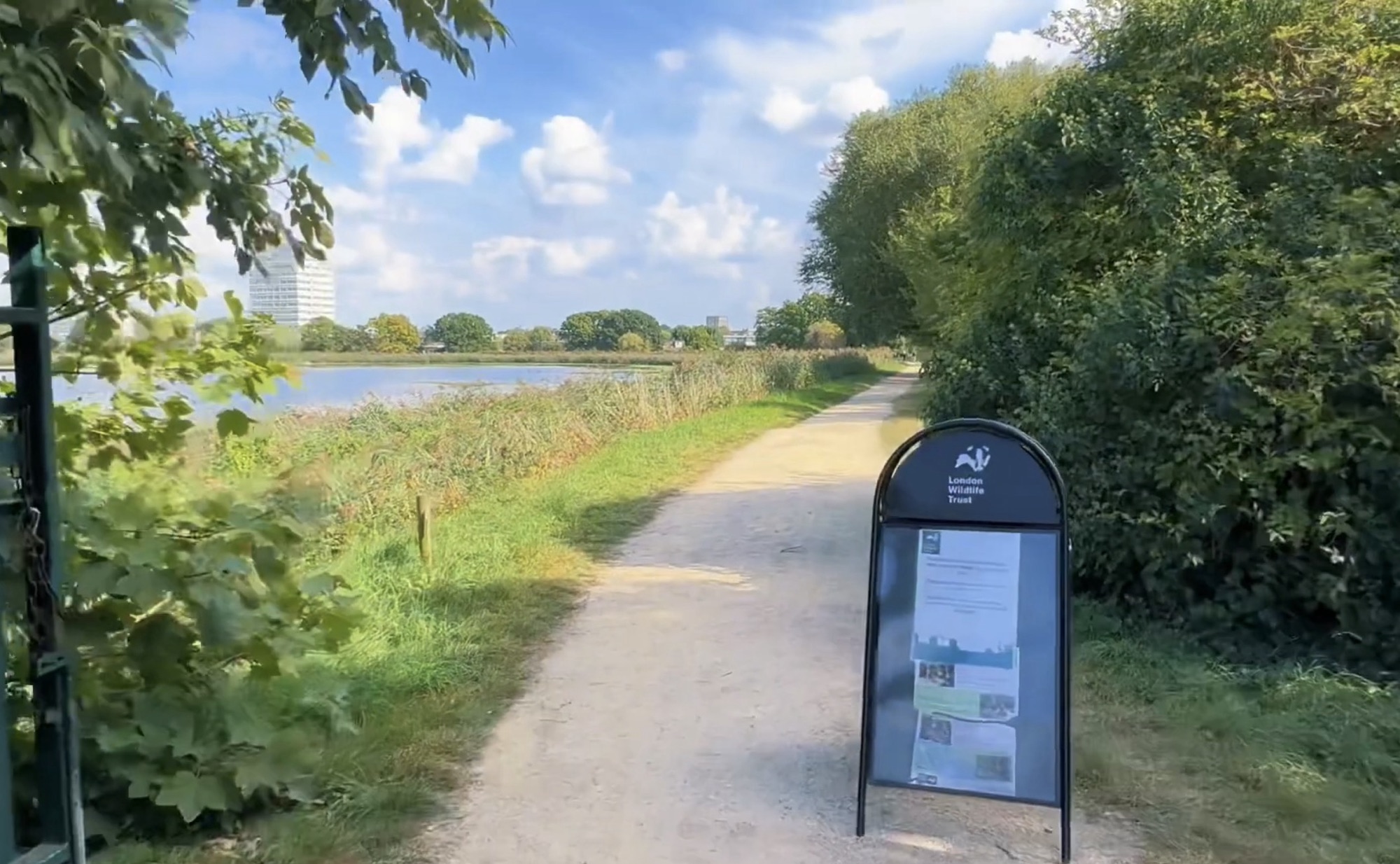 London Wildlife Trust A-frame information board on a gravel path beside the reservoir and reed beds